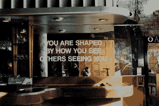 Text on a large mirror that reads: You are shaped by how you see others seeing you.